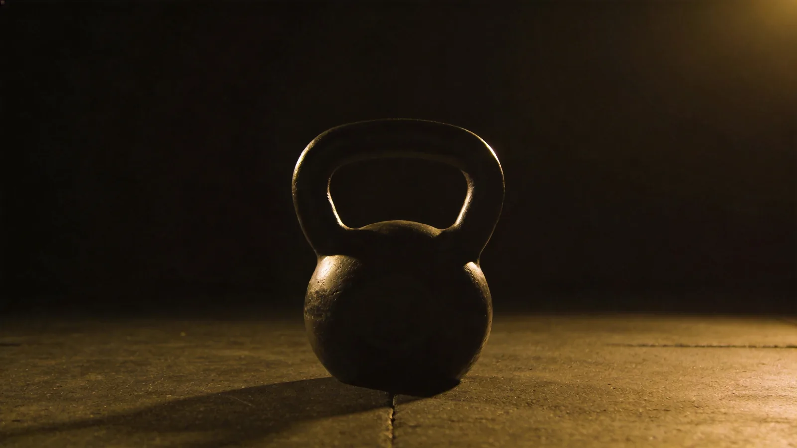 A single kettlebell lit on a dark gym floor